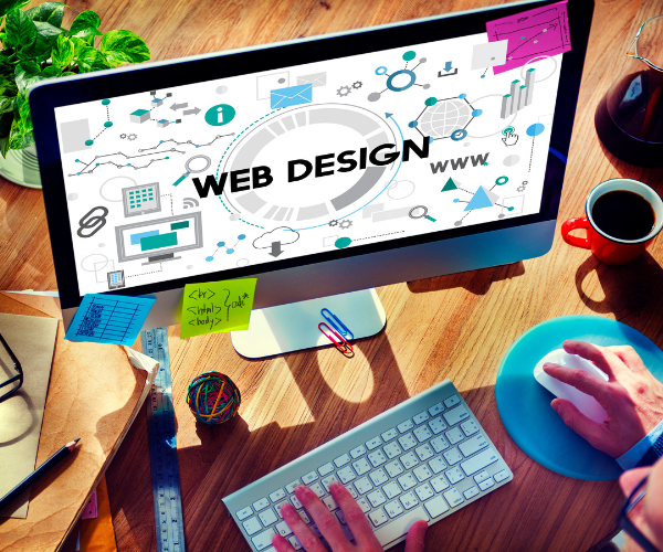 Scrivania di un web designer con monitor che mostra il layout per la creazione di siti web.